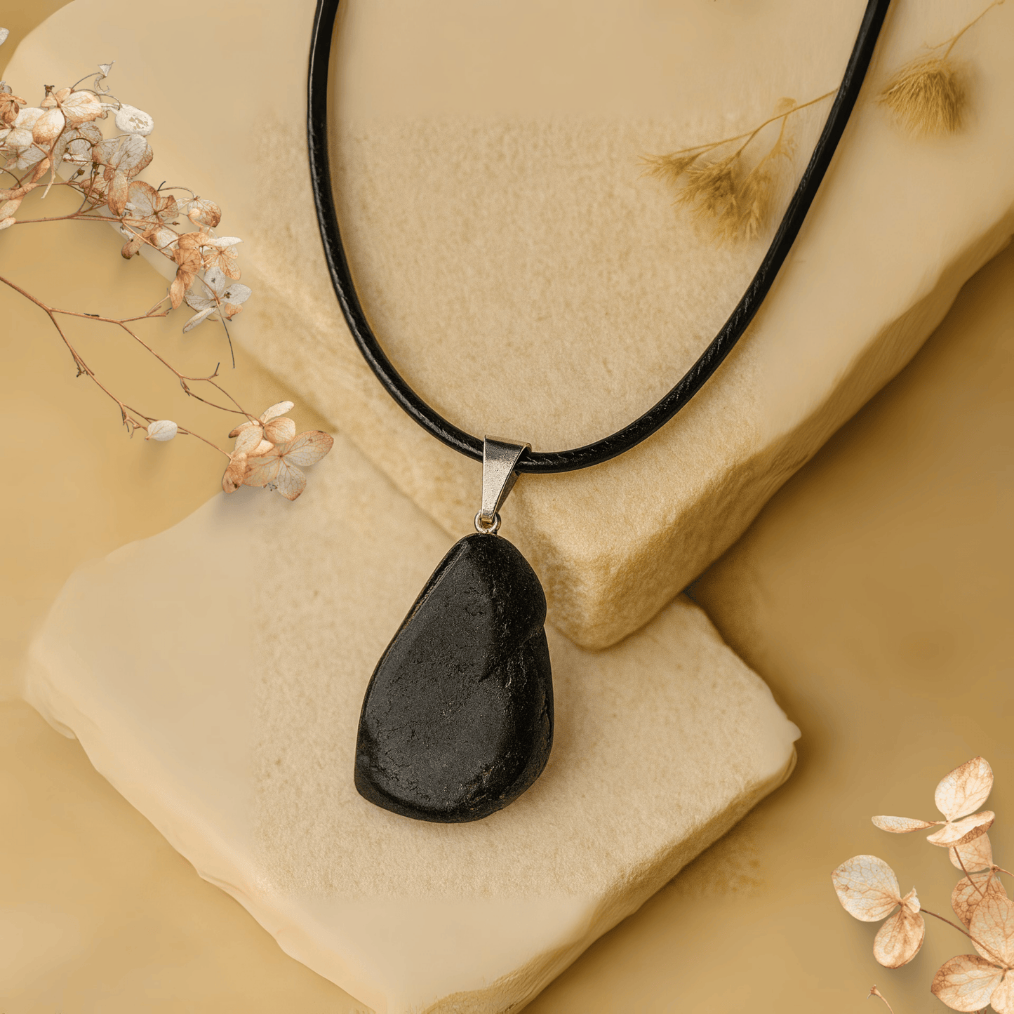 Black tourmaline pendant necklace on a beige stone with dried flowers