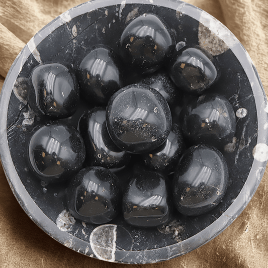 Close-up of a circular stone bowl with Black Obsidian tumblestones on a beige fabric background