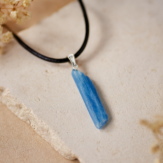 Blue Kyanite pendant necklace on a beige surface with dried flowers
