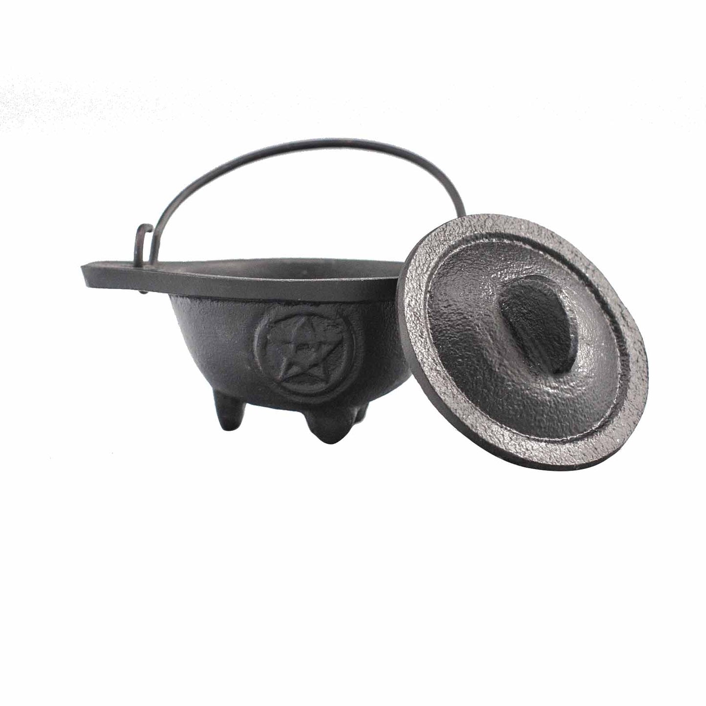 Small black cauldron with a carved pentagram in a circle on the front of it and with the lid laying next to it on a white background