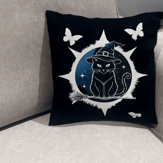 Black pillow with a cat in a witch's hat design on a gray couch.