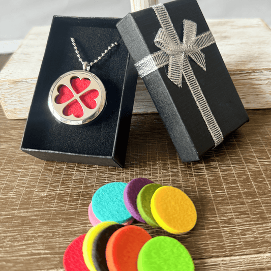 Necklace with a red heart pendant in a black box, surrounded by colorful felt pads on a wooden surface.