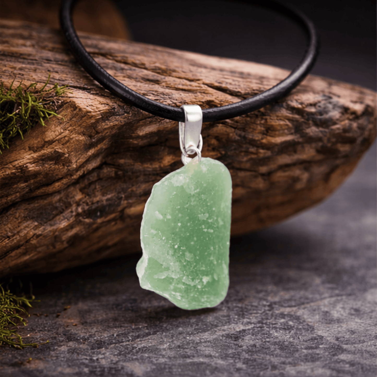 Green quartz raw crystal on a black cord necklace draped over a wooden log