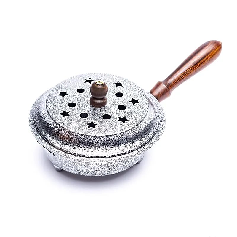 Closed silver iron incense burner pot with lid which has moon and stars cut out of it and a wooden handle on a white background