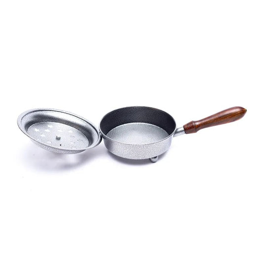 A silver iron incense burner pot with lid which has moon and stars cut out of it and a wooden handle on a white background
