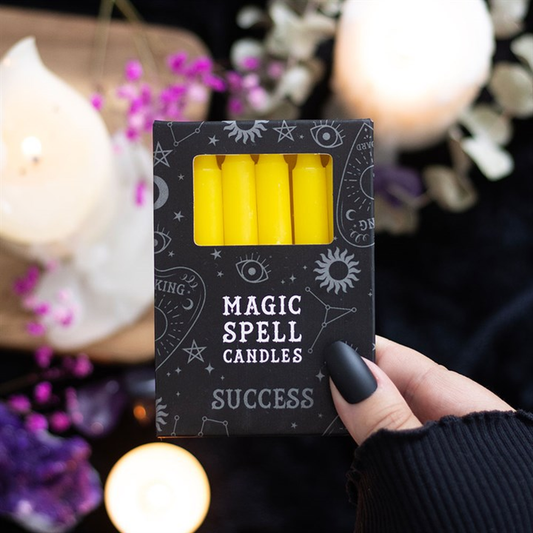 Box of 'Magic Spell Candles' labeled 'Success' held by a hand with a blurred candlelit background.