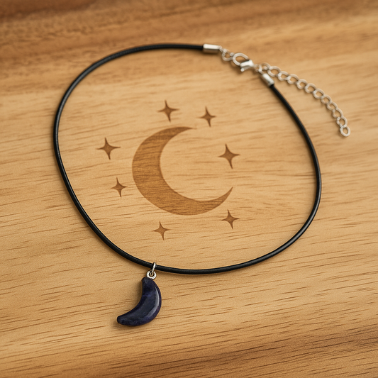 Amethyst crescent moon pendant on a black faux leather cord necklace which has a little extension chain on lobster clasp closing. This necklace is laying on an oak table with a crescent moon and stars engraved on the table.
