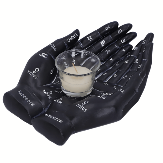 Black resin hands with astrological symbols holding a small glass container with a candle on a white background