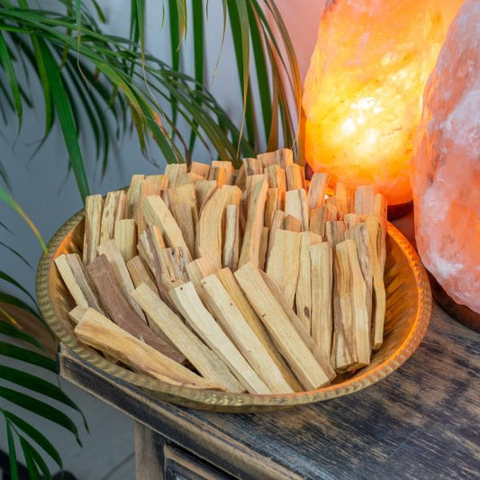 Palo Sticks on a table in a brass bowl and salt lamps and plant in the background