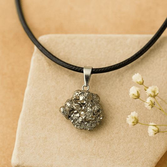 Necklace with a rough pyrite (fools gold) pendant on a black cord chain on a beige background