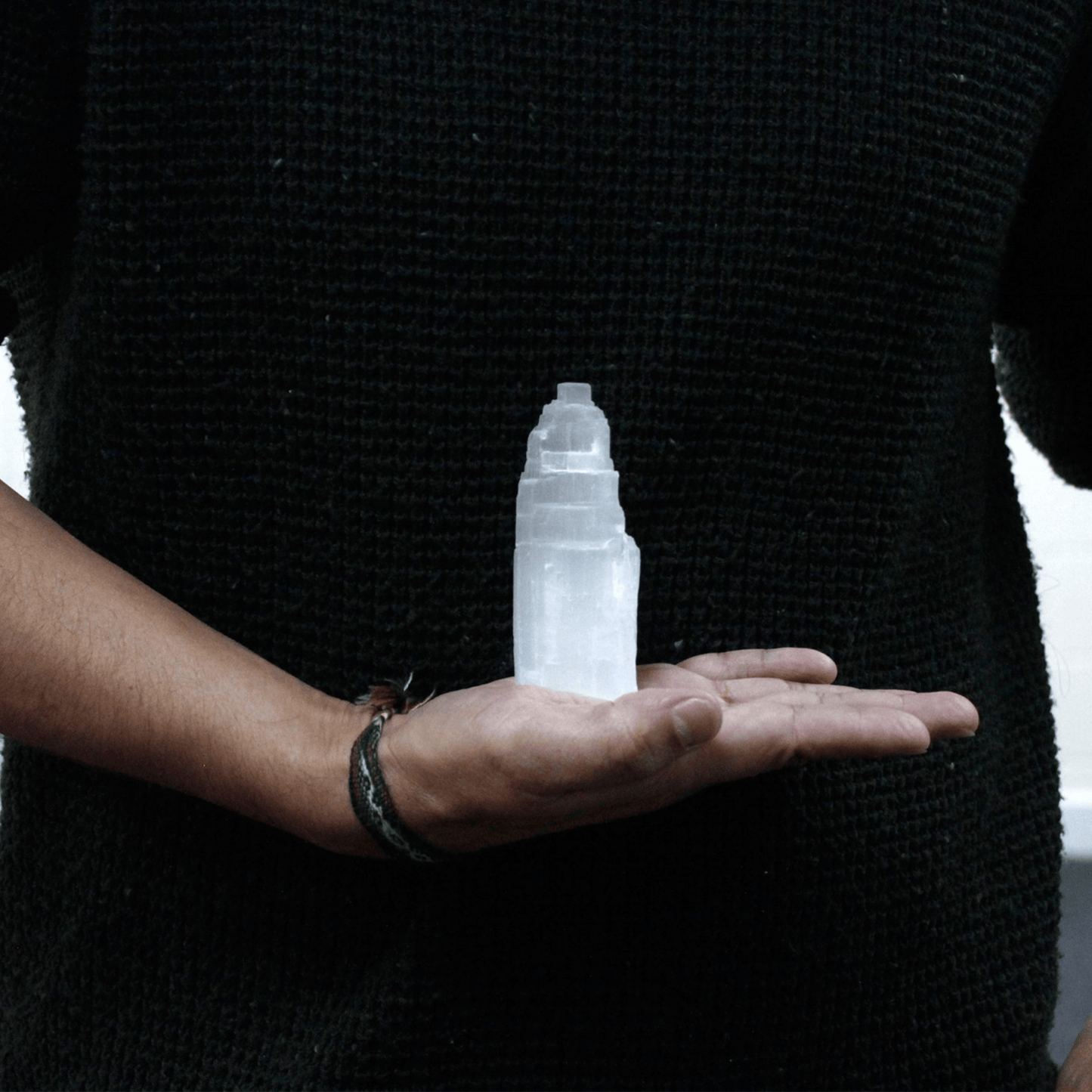 Person holding a white selenite ice berg 10cm in their palm against a black jumper.
