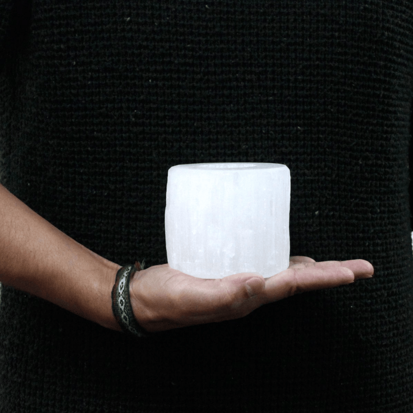 Person holding a textured white selenite cylinder shaped candle holder in front of a black background