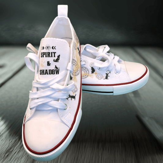 White sneakers with witchy black text and graphics on a wooden surface