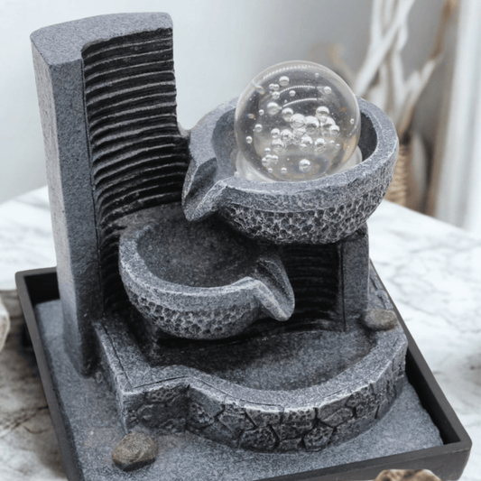 Decorative stone fountain with a glass ball on top, placed on a white surface.