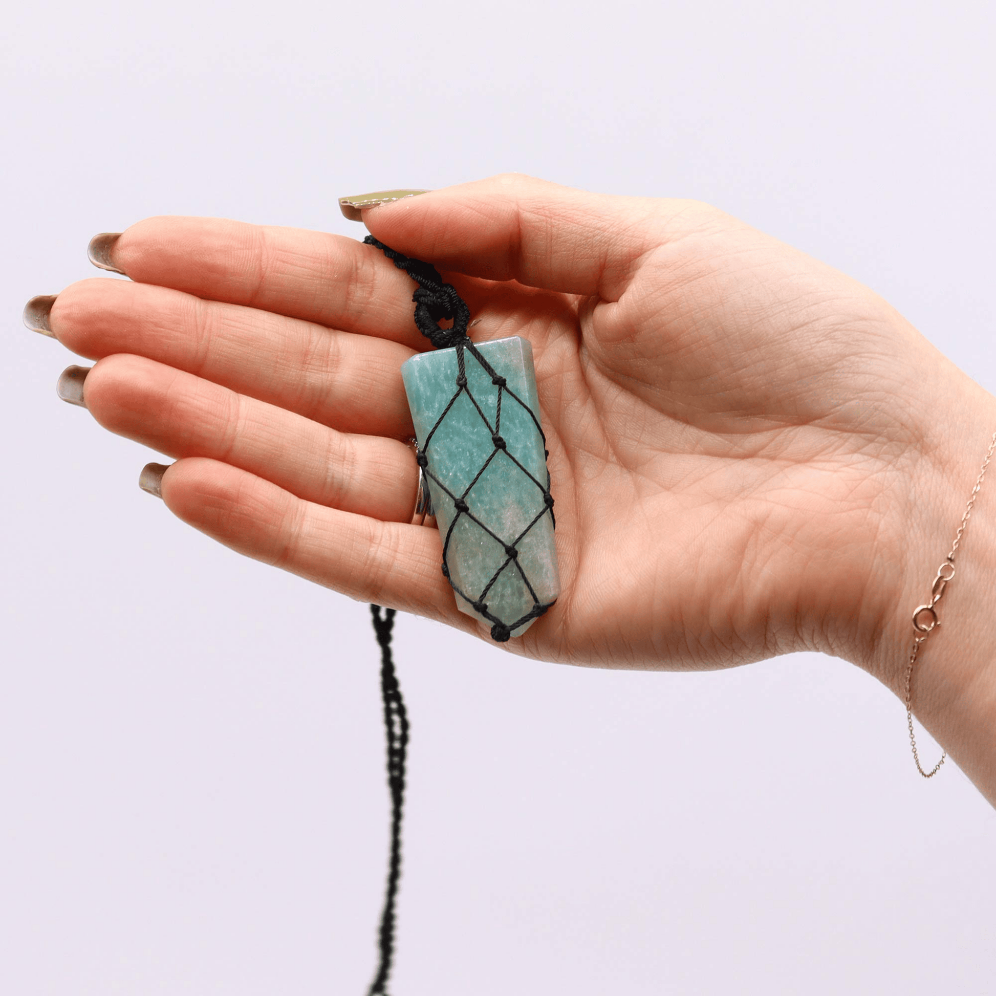 Hand holding a necklace with a turquoise pendant against a light background