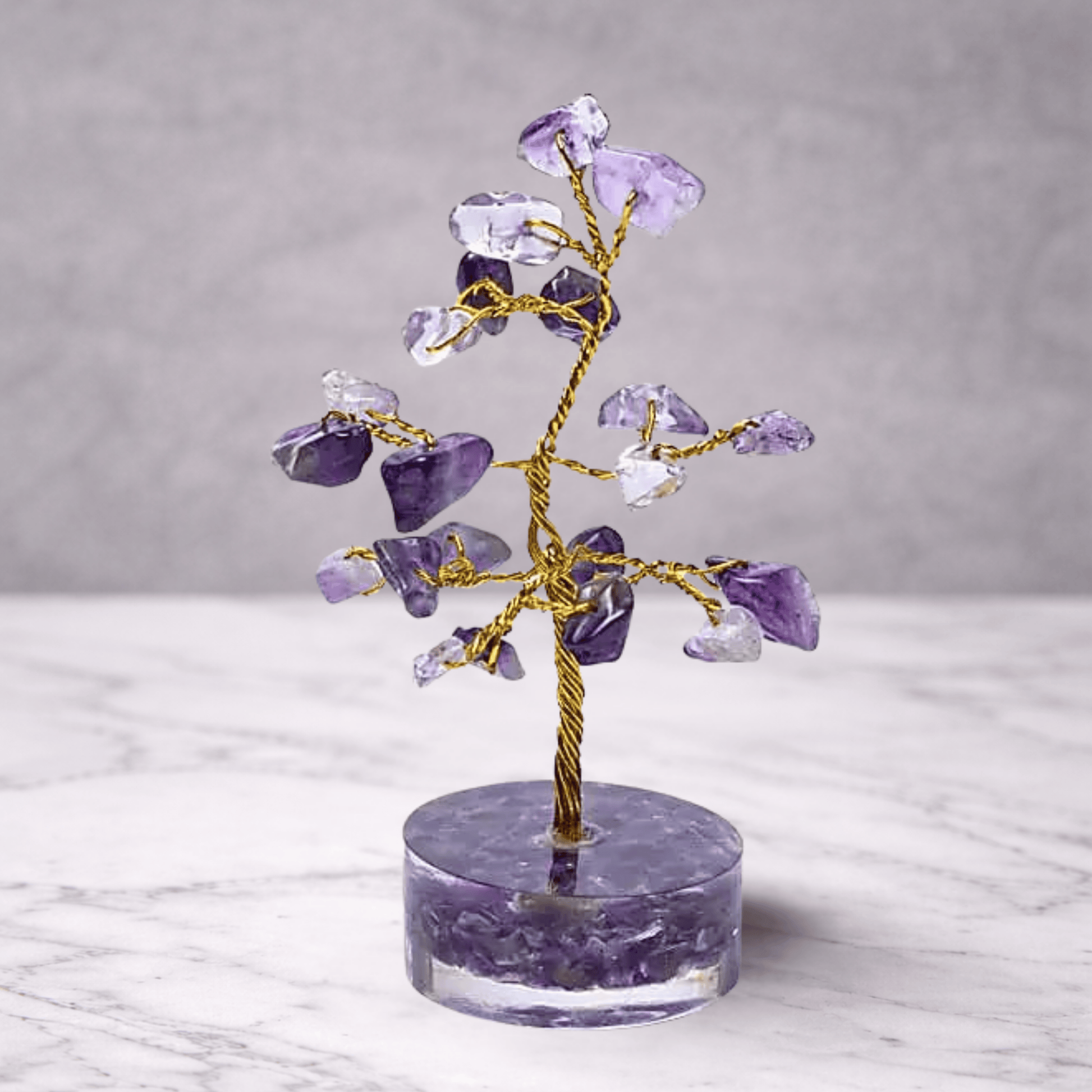 Crystal tree with purple and clear stones on a marble base against a gray background