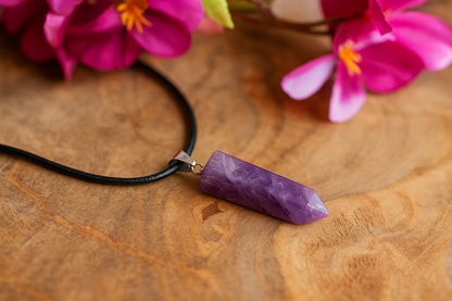 Purple stone pendant on a black cord with pink flowers in the background on a wooden surface