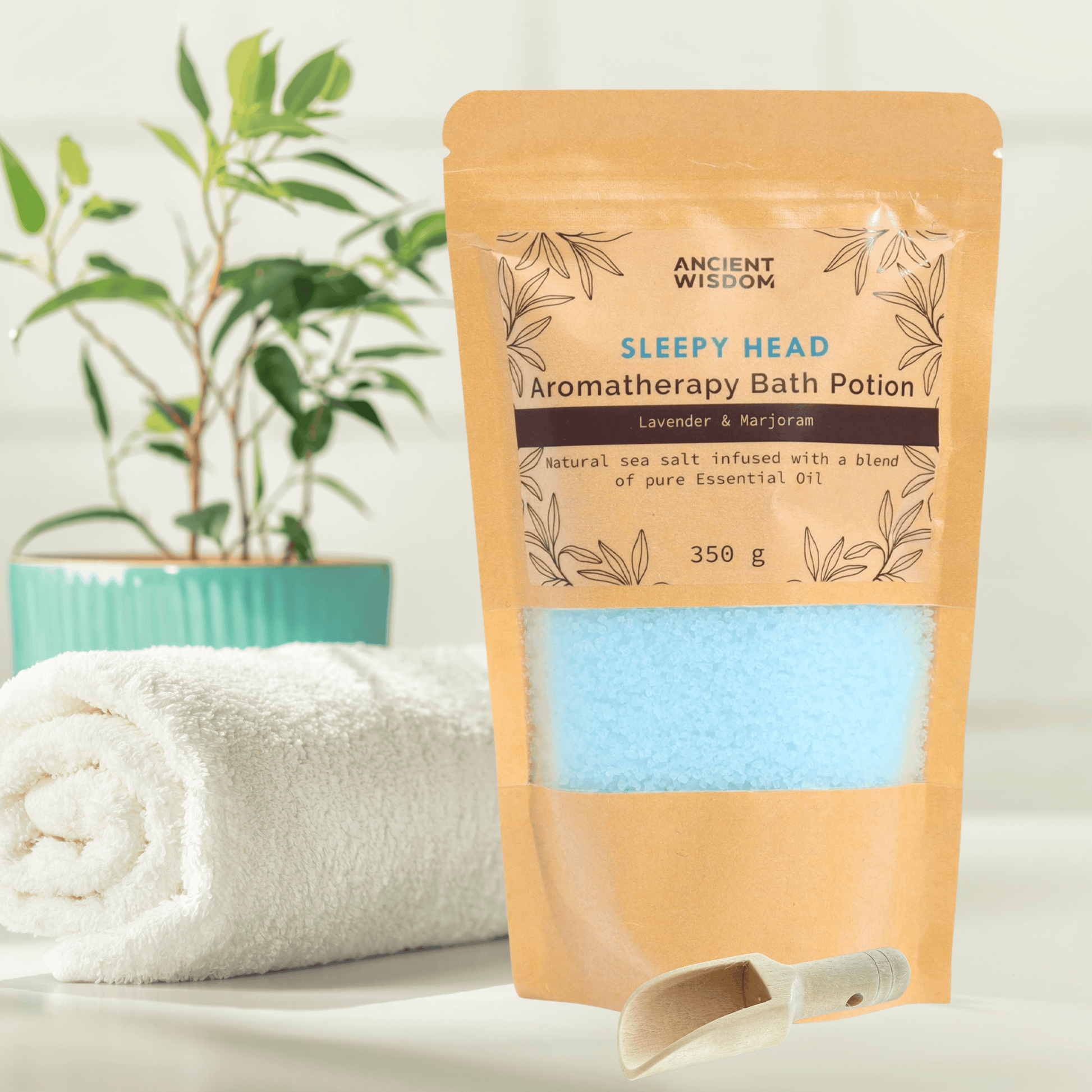 A kraft bag containing light blue Aromatherapy sea salt bath potion in a bathroom setting with a rolled up white towel and a green plant in the background.