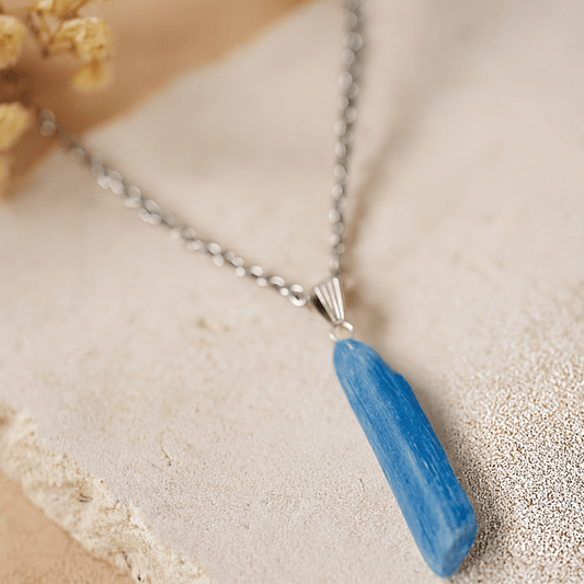 Necklace with a blue Kyanite pendant on a sandy coloured stone surface