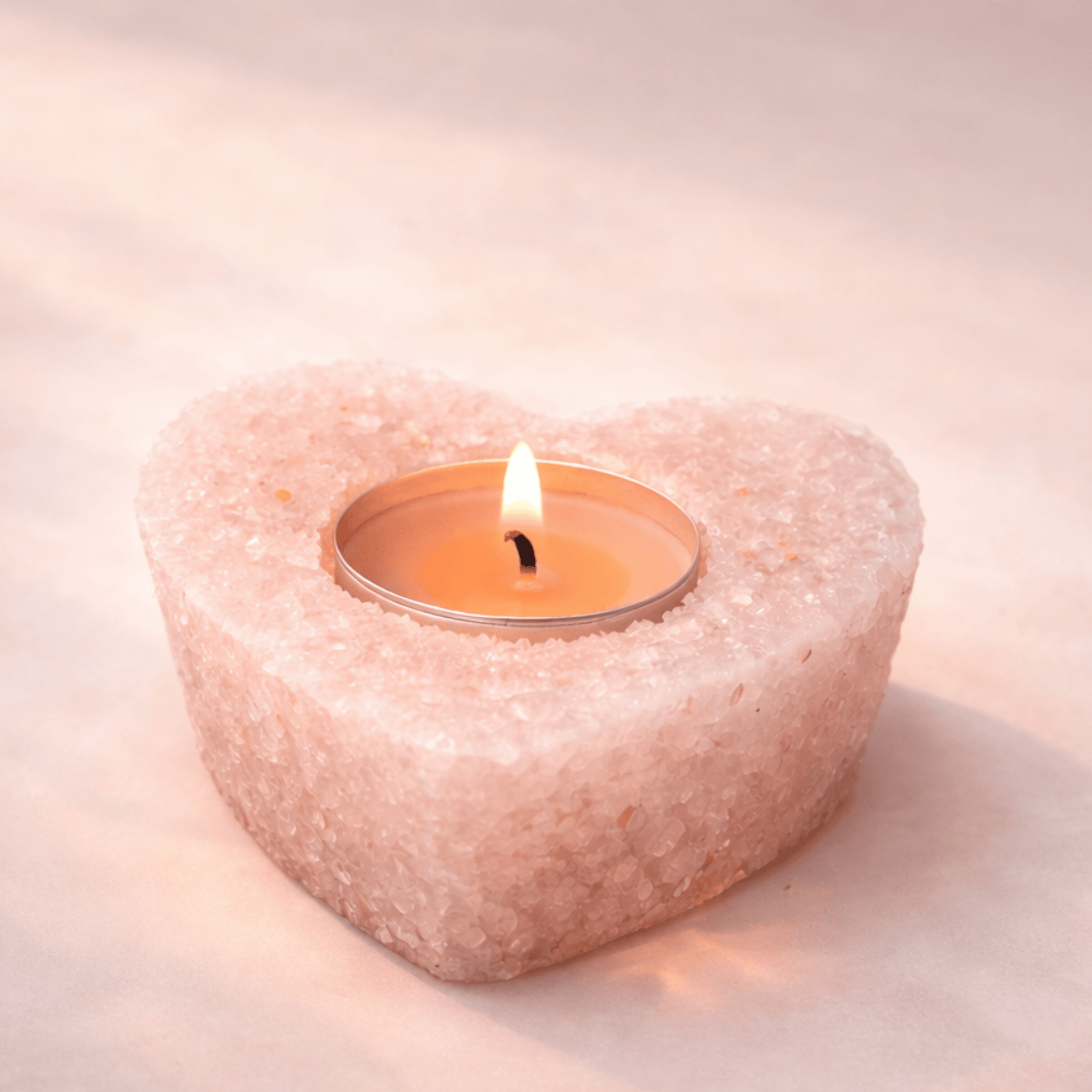 Heart-shaped stone candle holder with a lit candle on a soft pink background