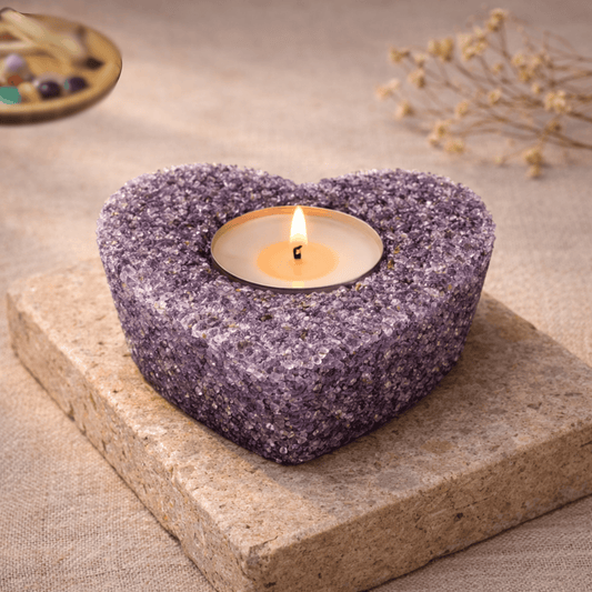 Heart-shaped purple Amethyst stone candle holder with a lit candle inside on a stone surface.