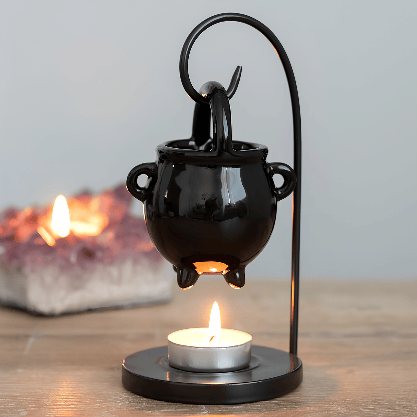 Black cauldron-shaped lantern with a lit candle inside on a wooden surface.