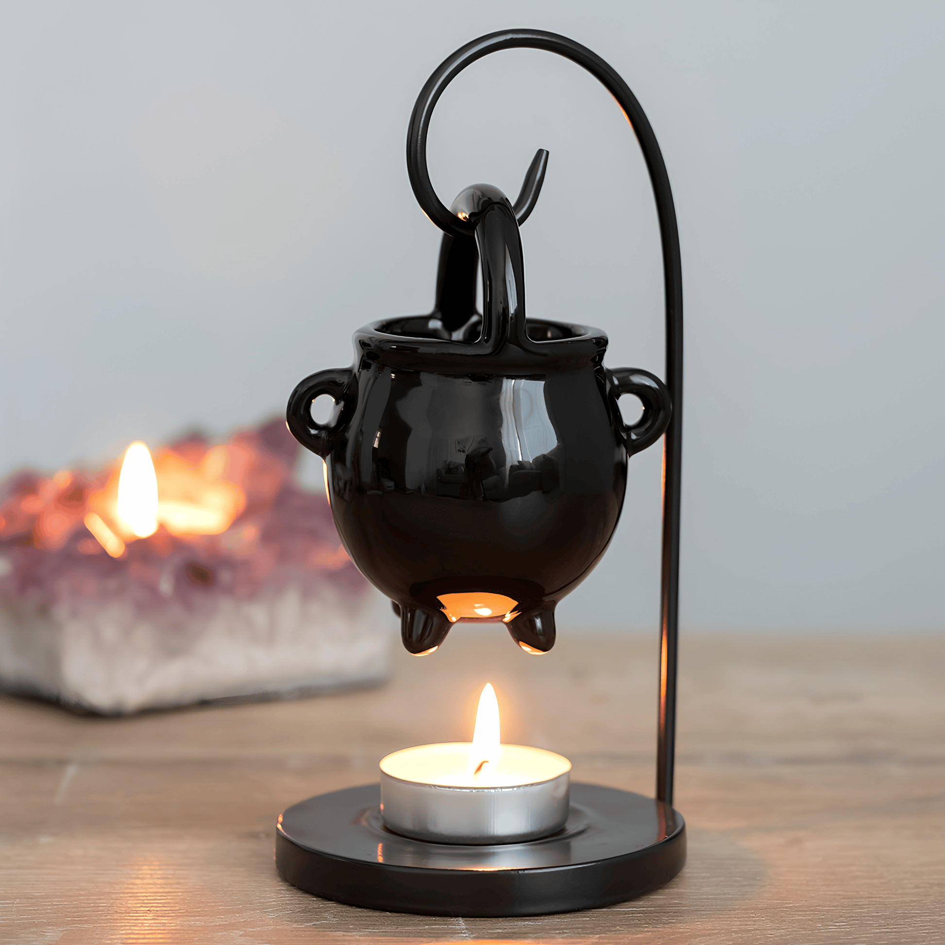 Black cauldron-shaped lantern with a lit candle inside on a wooden surface.