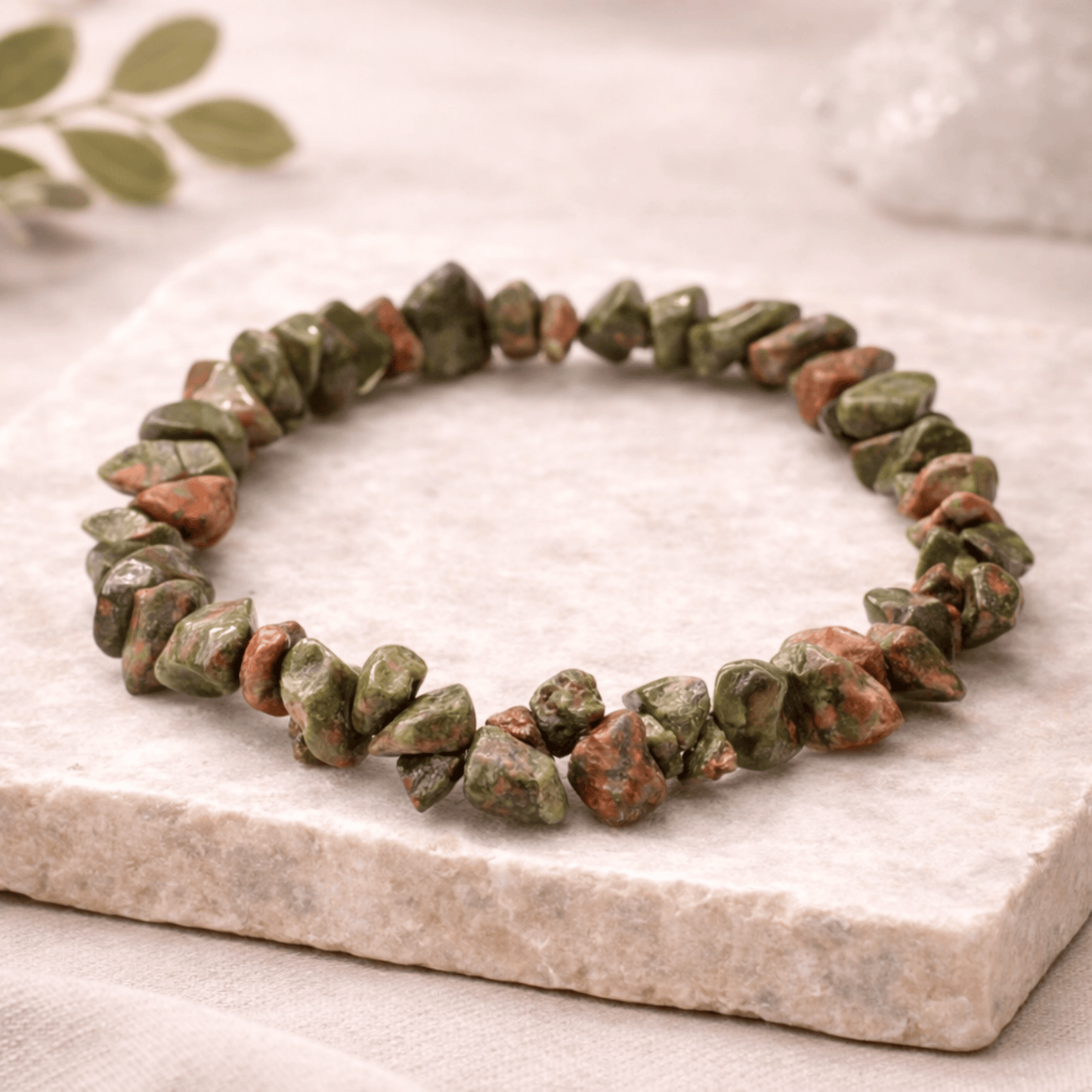 Green and brown stone bracelet on a marble surface with a leafy background