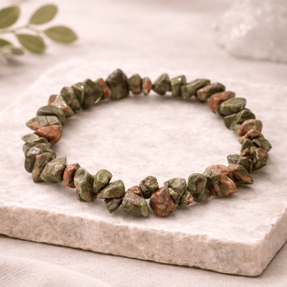 Green and brown stone bracelet on a marble surface with a leafy background