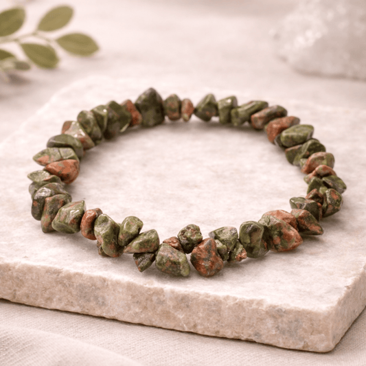 Green and brown stone bracelet on a marble surface with a leafy background
