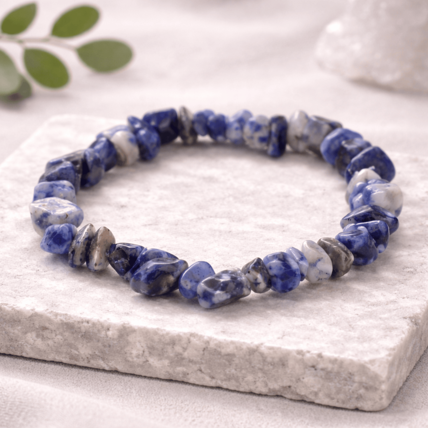 Blue and grey and white chipstone bracelet laying on a marble stone square on a white background