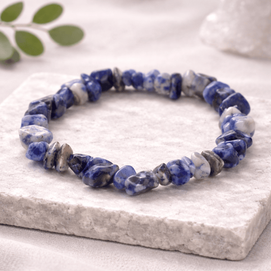 Blue and grey and white chipstone bracelet laying on a marble stone square on a white background