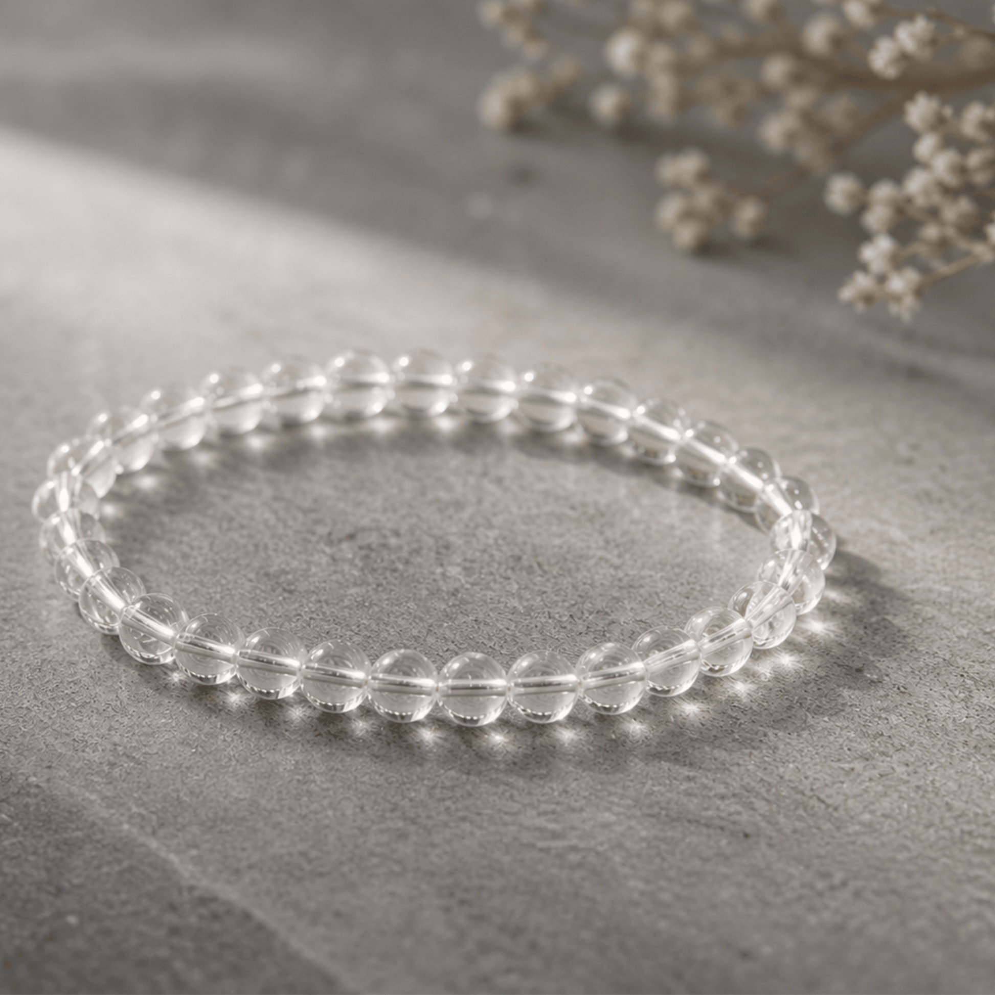 Clear beaded bracelet on a gray surface with light-colored flowers in the background
