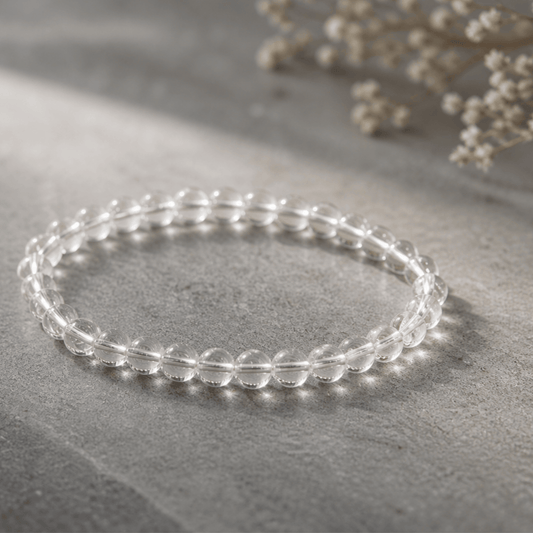 Clear beaded bracelet on a gray surface with light-colored flowers in the background
