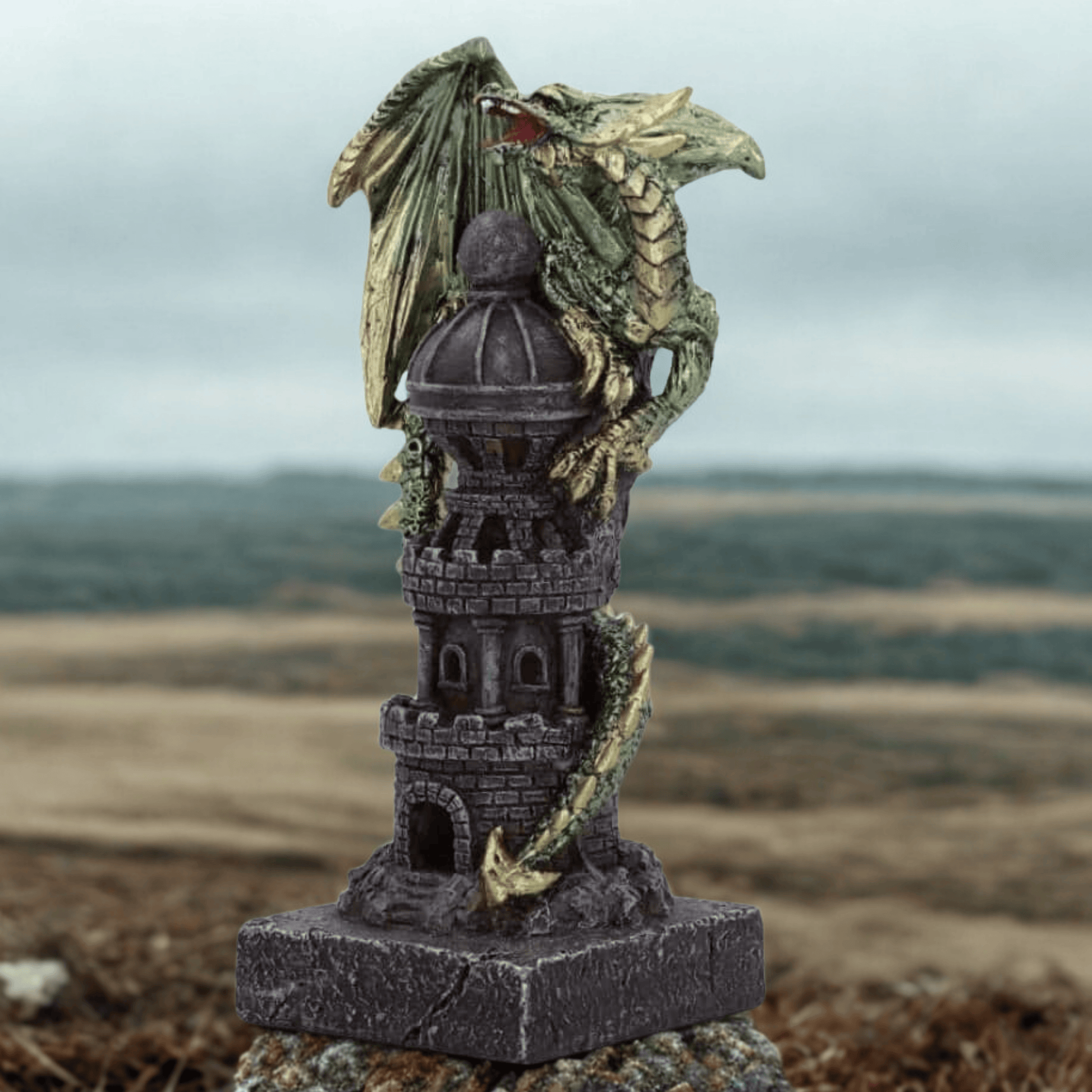Decorative figurine of a dragon on top of a castle tower with a blurred landscape in the background.