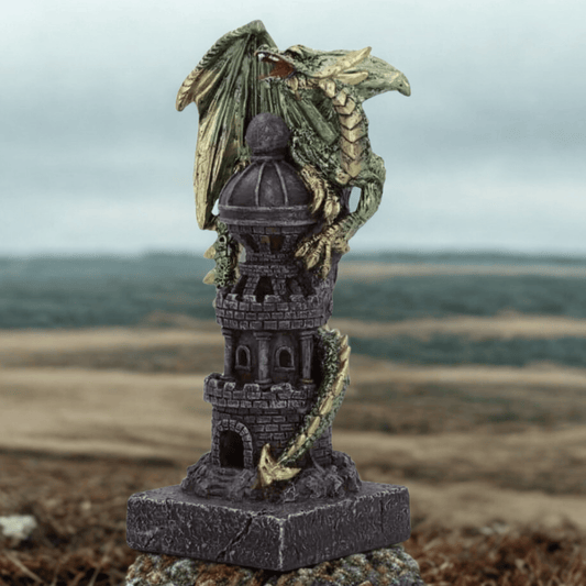 Decorative figurine of a dragon on top of a castle tower with a blurred landscape in the background.