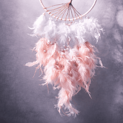 Pink and white dreamcatcher with feathers against a dark background