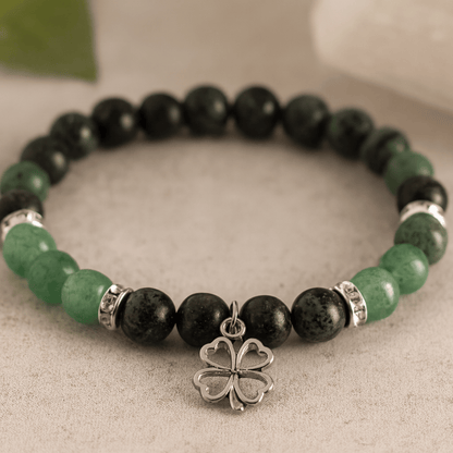 Bracelet with black and green beads and a silver four-leaf clover charm on a neutral background