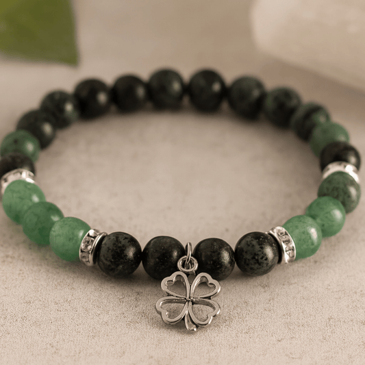 Bracelet with black and green beads and a silver four-leaf clover charm on a neutral background