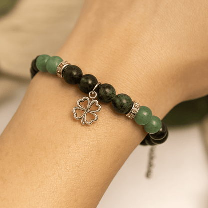 Bracelet with green and black beads and a silver four-leaf clover charm on a wrist.