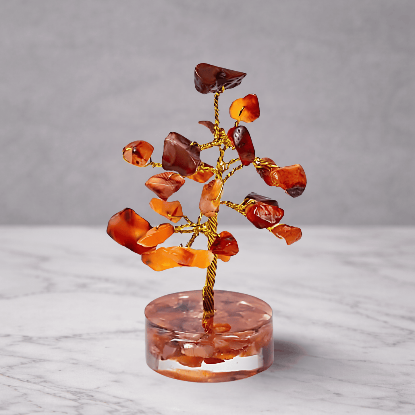 Crystal tree with red and orange stones on a clear base against a gray background