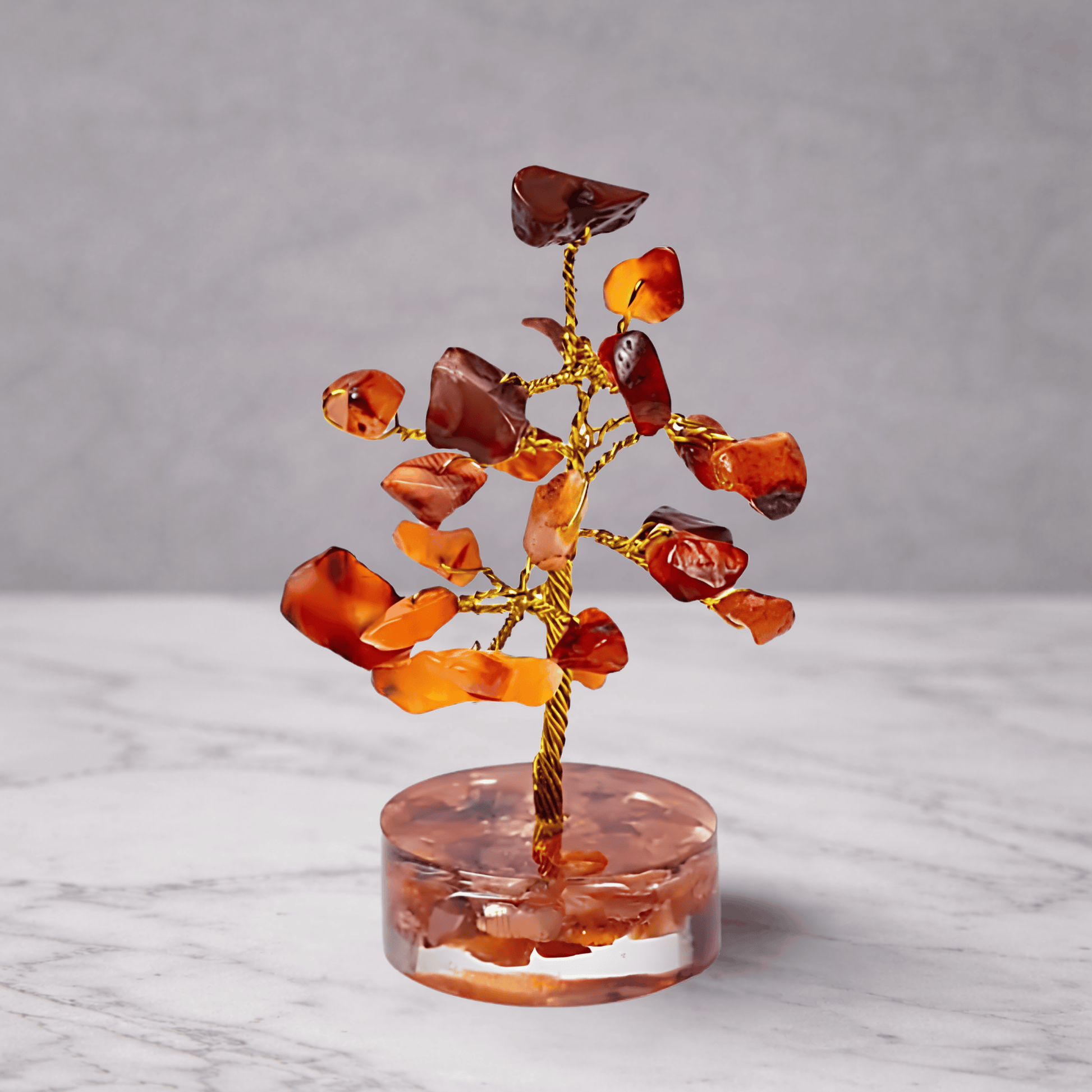 Crystal tree with red and orange stones on a clear base against a gray background