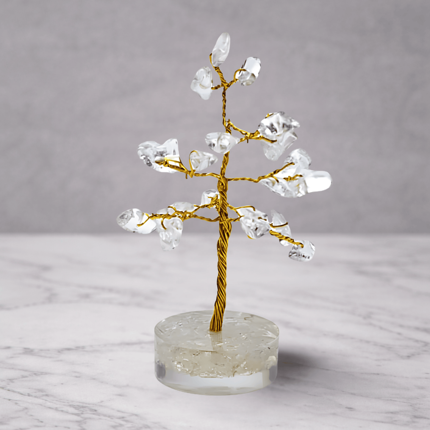 Crystal tree on a clear base with a gold trunk against a gray background