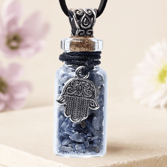 Necklace with a small glass bottle containing blue Lapis Lazuli stones and a Hamsa hand pendant, against a blurred floral background.