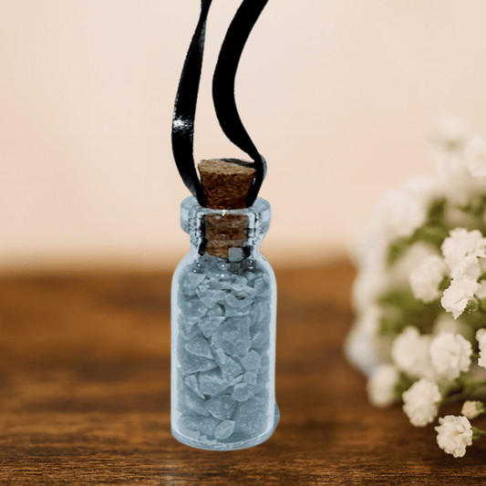 Small glass bottle with cork lid on a black cord, against a blurred background with flowers.