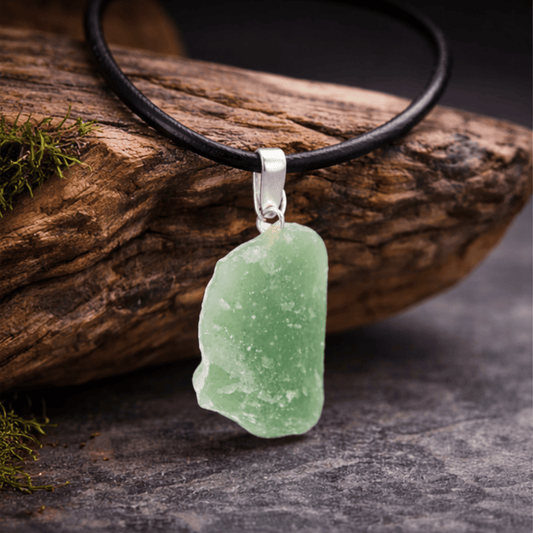Green quartz raw crystal on a black cord necklace draped over a wooden log