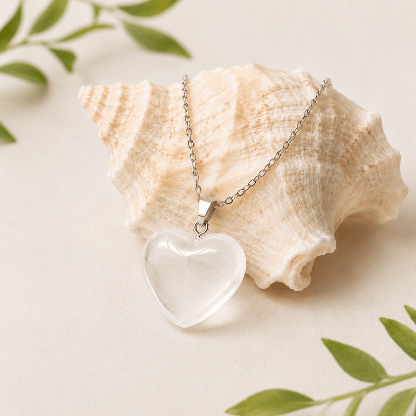 Heart-shaped clear pendant necklace on a shell with green leaves in the background