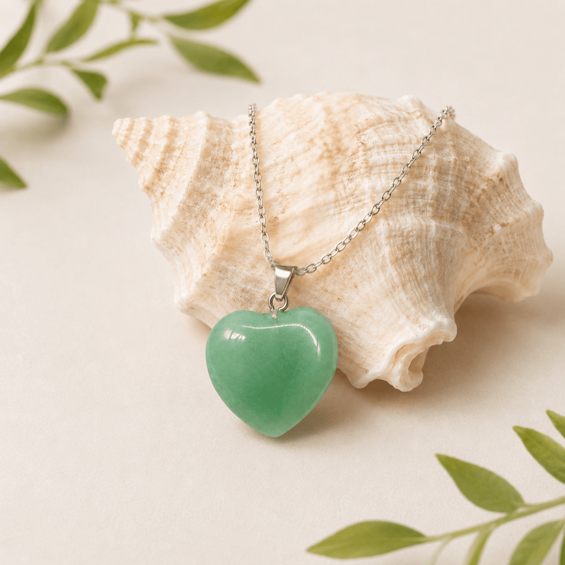 Green heart-shaped pendant on a chain with a shell and leaves in the background