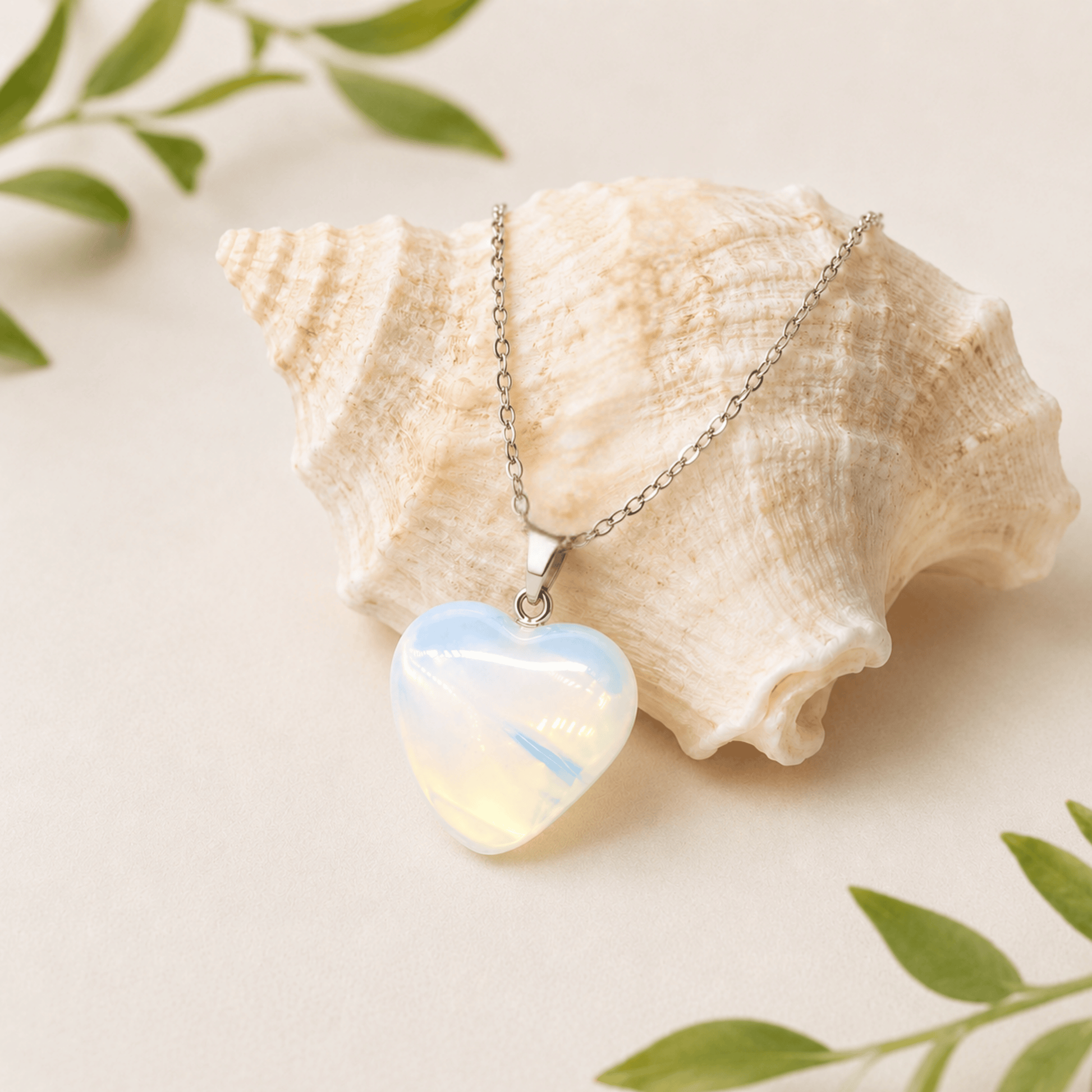 Heart-shaped opal pendant on a chain with a seashell and green leaves in the background