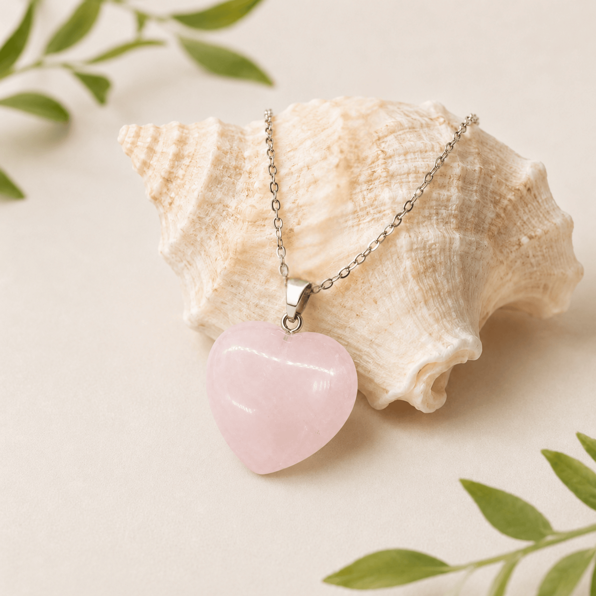 Heart-shaped pink pendant necklace on a seashell with green leaves in the background